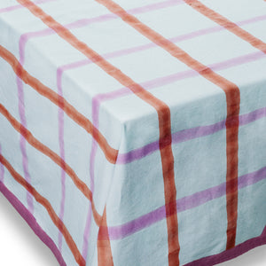 Table cloth with subtle mint green gingham pattern, overlaid with stripes in shades of burnt orange and muted pink, and finished with a deep purple hem