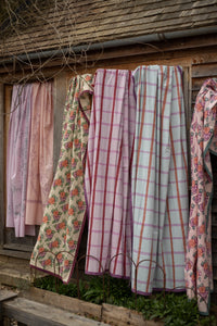 Several patterned fabrics hang from a clothesline against a rustic wooden wall.