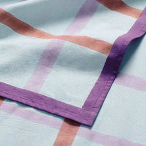 Table cloth with subtle mint green gingham pattern, overlaid with stripes in shades of burnt orange and muted pink, and finished with a deep purple hem